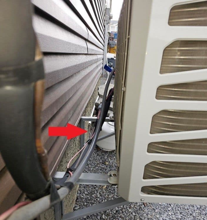 Close-up of lines and wiring running at an angle behind an outdoor unit, marked with a red arrow.