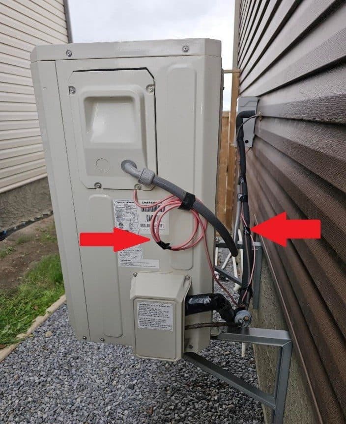 The back of an outdoor unit with wiring looped loosely and lines not fastened to the wall, marked with red arrows.