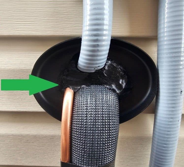 Insulated refrigerant lines passing through a wall sleeve on vinyl siding, sealed around the opening.