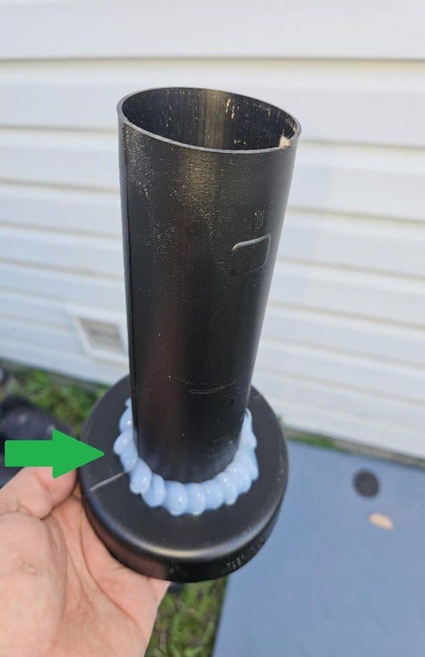 A black plastic wall sleeve held in a hand, with a bead of sealant around its flange.